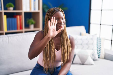 Photo for African american woman sitting on sofa saying hello with hand at home - Royalty Free Image