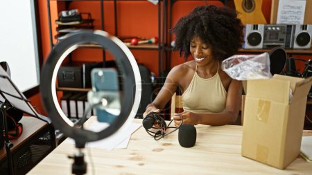 Foto de Mujer afroamericana reportera de radio grabando video desempacando micrófono de caja de cartón en estudio de radio - Imagen libre de derechos