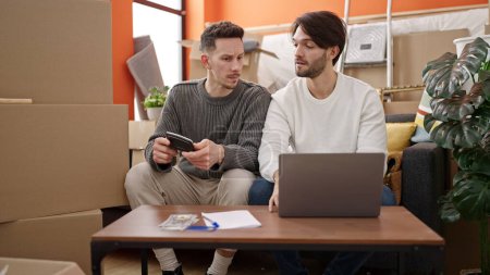 Foto de Dos hombres en pareja usando laptop contando dólares en casa nueva - Imagen libre de derechos