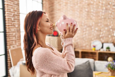 Photo for Young caucasian woman smiling confident holding piggy bank at new home - Royalty Free Image