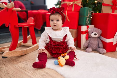 Photo for Adorable blonde toddler sitting on floor by christmas gifts at home - Royalty Free Image