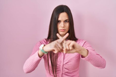 Photo for Young hispanic woman standing over pink background rejection expression crossing fingers doing negative sign - Royalty Free Image