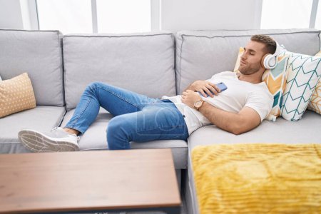 Téléchargez les photos : Young caucasian man listening to music lying on sofa at home - en image libre de droit