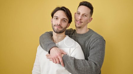 Foto de Dos hombres se abrazan de pie con expresión relajada sobre un fondo amarillo aislado - Imagen libre de derechos