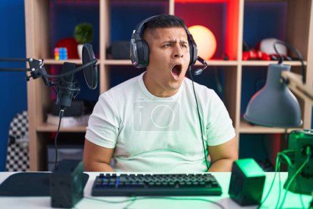 Photo for Young hispanic man playing video games angry and mad screaming frustrated and furious, shouting with anger. rage and aggressive concept. - Royalty Free Image