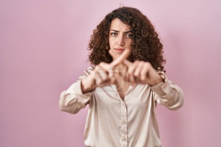 Photo for Hispanic woman with curly hair standing over pink background rejection expression crossing fingers doing negative sign - Royalty Free Image