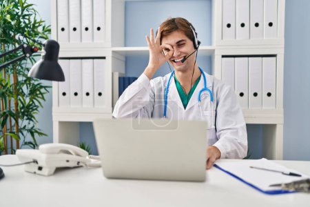 Photo for Young doctor man working on online appointment smiling happy doing ok sign with hand on eye looking through fingers - Royalty Free Image