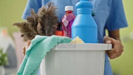 Foto de Mujer afroamericana limpiadora profesional que sostiene la cesta con productos en la sala de lavandería - Imagen libre de derechos