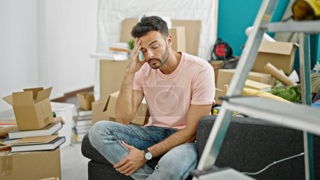 Photo for Young hispanic man sitting on sofa with serious expression at new home - Royalty Free Image