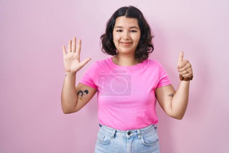 Téléchargez les photos : Jeune femme hispanique debout sur fond rose montrant et pointant vers le haut avec les doigts numéro six tout en souriant confiant et heureux. - en image libre de droit