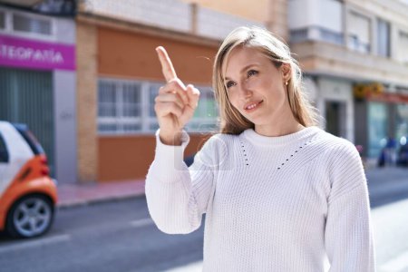 Téléchargez les photos : Jeune femme blonde souriante confiante pointant du doigt la rue - en image libre de droit