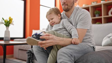 Téléchargez les photos : Père et fils assis sur le canapé portant des chaussures à la maison - en image libre de droit
