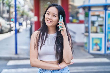 Téléchargez les photos : Jeune femme chinoise souriant confiant parler sur le smartphone à la rue - en image libre de droit