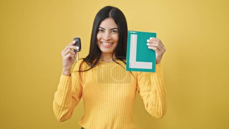 Photo for Young beautiful hispanic woman holding key of new car and new driver license over isolated yellow background - Royalty Free Image