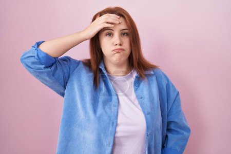 Photo for Young hispanic woman with red hair standing over pink background worried and stressed about a problem with hand on forehead, nervous and anxious for crisis - Royalty Free Image