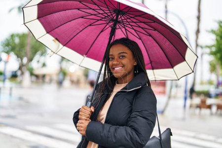 Téléchargez les photos : African american woman smiling confident using umbrella at street - en image libre de droit