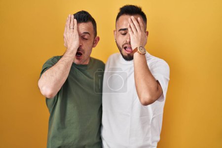 Téléchargez les photos : Couple homosexuel debout sur fond jaune bâillant fatigué couvrant la moitié du visage, des yeux et de la bouche avec la main. mal au visage dans la douleur. - en image libre de droit