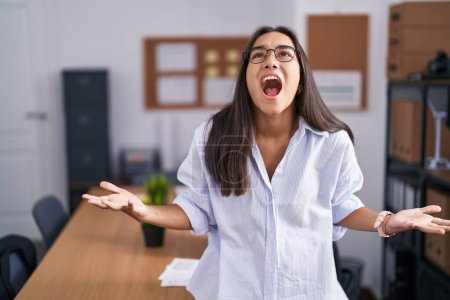 Téléchargez les photos : Jeune femme hispanique au bureau en colère et folle criant frustrée et furieuse, criant de colère. rage et concept agressif. - en image libre de droit