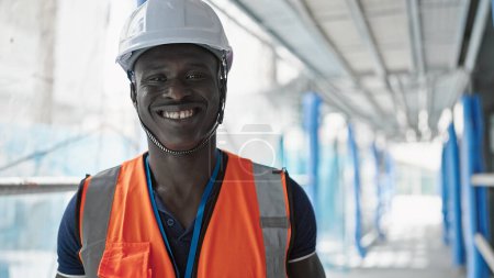 Foto de Africano americano hombre constructor sonriendo confiado tomando gafas fuera en construcción lugar - Imagen libre de derechos