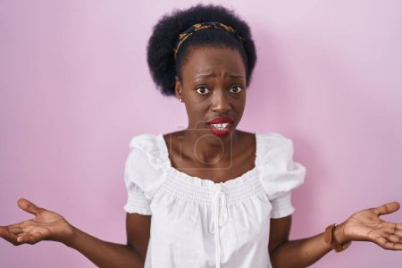 Photo for African woman with curly hair standing over pink background clueless and confused with open arms, no idea concept. - Royalty Free Image
