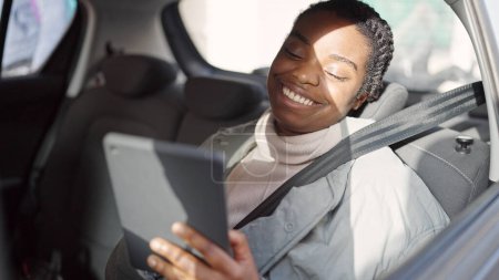 Téléchargez les photos : Afro-américaine femme à l'aide touchpad assis sur la voiture à la rue - en image libre de droit
