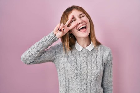 Téléchargez les photos : Beautiful woman standing over pink background doing peace symbol with fingers over face, smiling cheerful showing victory - en image libre de droit