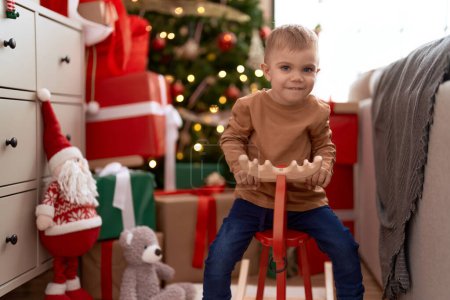 Photo for Adorable toddler playing on reindeer rocking by christmas tree at home - Royalty Free Image