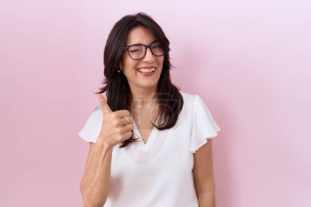 Photo for Middle age hispanic woman wearing casual white t shirt and glasses doing happy thumbs up gesture with hand. approving expression looking at the camera showing success. - Royalty Free Image