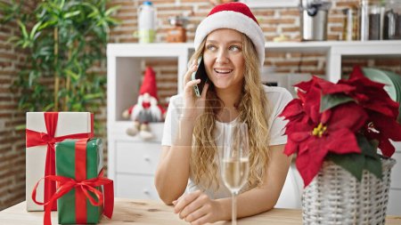 Téléchargez les photos : Jeune femme blonde célébrant Noël parler sur smartphone boire du champagne à la salle à manger - en image libre de droit