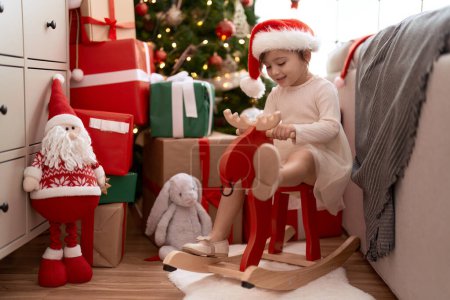 Foto de Adorable chica sentada en rockero renos por árbol de Navidad en casa - Imagen libre de derechos