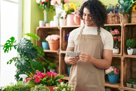 Téléchargez les photos : Jeune homme latin fleuriste souriant confiant compter les dollars à la boutique de fleurs - en image libre de droit