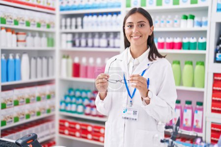 Photo for Young beautiful hispanic woman pharmacist smiling confident holding glasses at pharmacy - Royalty Free Image