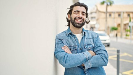 Téléchargez les photos : Jeune homme hispanique souriant confiant debout avec les bras croisés geste à la rue - en image libre de droit