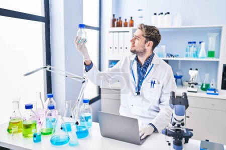 Foto de Científico joven usando portátil sosteniendo botella en el laboratorio - Imagen libre de derechos