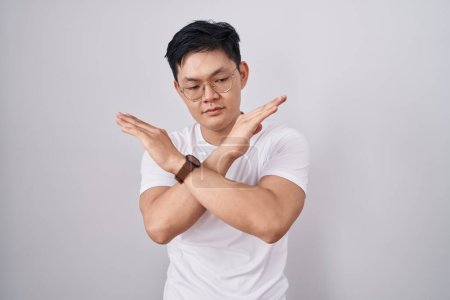 Foto de Joven asiático hombre de pie sobre blanco fondo rechazo expresión cruzar brazos haciendo negativo signo, enojado cara - Imagen libre de derechos