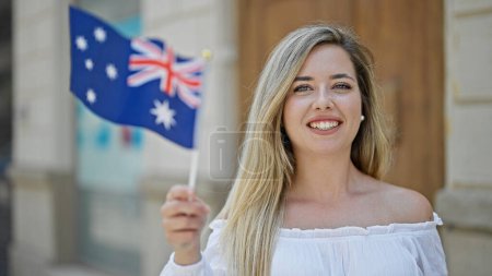 Photo for Young blonde woman smiling confident holding australia flag at street - Royalty Free Image