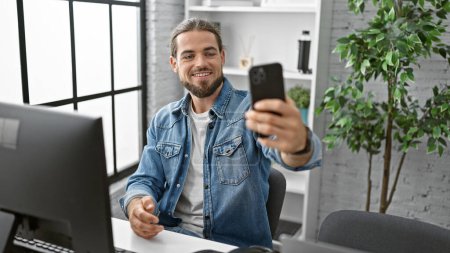 Téléchargez les photos : Jeune homme d'affaires hispanique travailleur faire selfie par smartphone souriant au bureau - en image libre de droit
