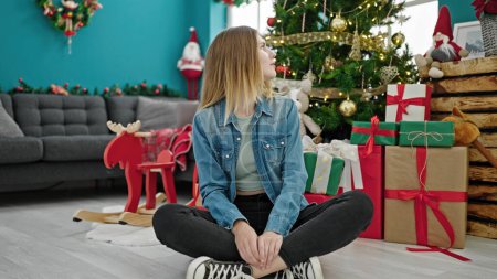 Foto de Mujer rubia joven celebrando la Navidad sentada en el suelo en casa - Imagen libre de derechos