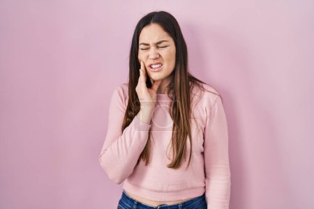 Téléchargez les photos : Young brunette woman standing over pink background touching mouth with hand with painful expression because of toothache or dental illness on teeth. dentist - en image libre de droit