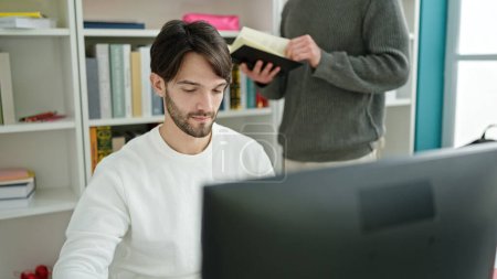 Foto de Dos hombres estudiantes usando libro de lectura por computadora estudiando en la universidad de la biblioteca - Imagen libre de derechos