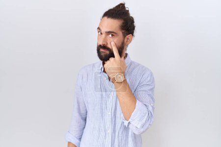 Téléchargez les photos : Homme hispanique avec barbe portant une chemise décontractée pointant vers l'œil vous regardant geste, expression suspecte - en image libre de droit