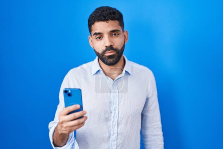 Téléchargez les photos : Homme hispanique avec barbe en utilisant le message de dactylographie smartphone l'air somnolent et fatigué, épuisé par la fatigue et la gueule de bois, les yeux paresseux le matin. - en image libre de droit