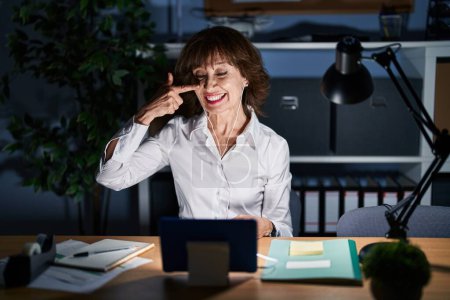 Photo for Middle age woman working at the office at night pointing with hand finger to face and nose, smiling cheerful. beauty concept - Royalty Free Image