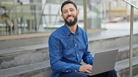 Téléchargez les photos : Jeune homme hispanique travailleur d'affaires en utilisant ordinateur portable assis sur les escaliers à la rue - en image libre de droit