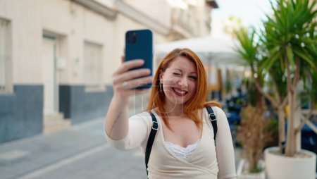 Foto de Joven pelirroja sonriendo confiada haciendo selfie por el teléfono inteligente en la calle - Imagen libre de derechos