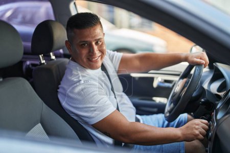 Téléchargez les photos : Jeune homme latin assis sur la voiture tournant sur la radio à la rue - en image libre de droit