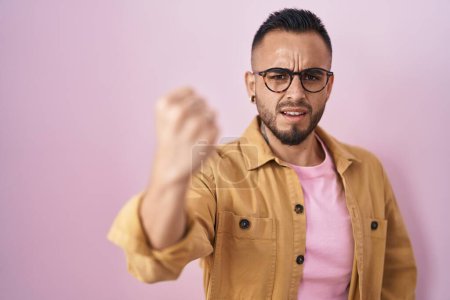 Photo for Young hispanic man standing over pink background angry and mad raising fist frustrated and furious while shouting with anger. rage and aggressive concept. - Royalty Free Image
