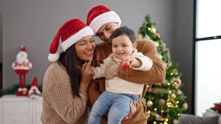 Foto de Pareja e hijo sosteniendo la bola de decoración de pie junto al árbol de Navidad en casa - Imagen libre de derechos