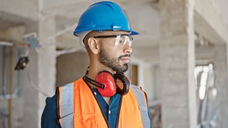 Téléchargez les photos : Jeune homme hispanique constructeur portant un casque de sécurité sur le chantier de construction - en image libre de droit