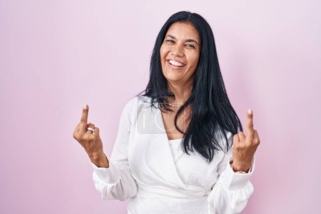 Foto de Mature hispanic woman standing over pink background showing middle finger doing fuck you bad expression, provocation and rude attitude. screaming excited - Imagen libre de derechos